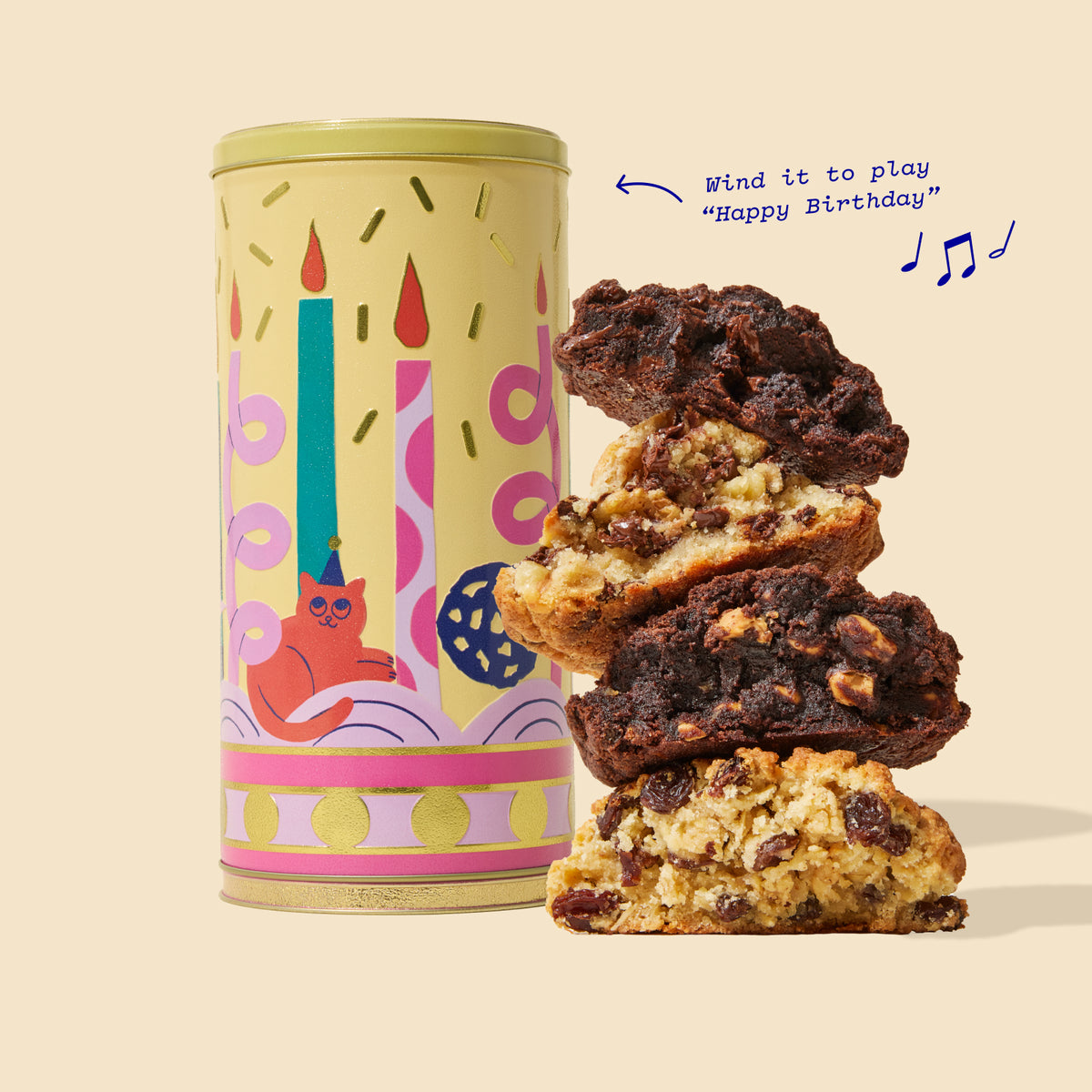 A decorative cylindrical tin of birthday cookies stands next to a stack of three broken chocolate chip cookies on a warm beige background. The tin is pale yellow with a birthday candle and cat illustration.